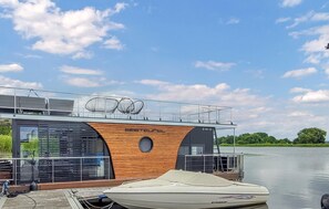 Un barco moderno con fachada de madera y cubierta protegida, amarrado en un río tranquilo.