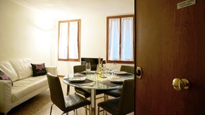 A dining area with a round glass table set for four, surrounded by chairs. There is a white sofa with a pillow in the background.