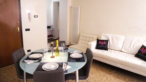 A dining area with a glass table, chairs, and a white sofa with black pillows.
