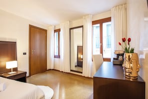 Una habitación de hotel con una cama, un escritorio con lámpara, un espejo y un jarrón con flores.
