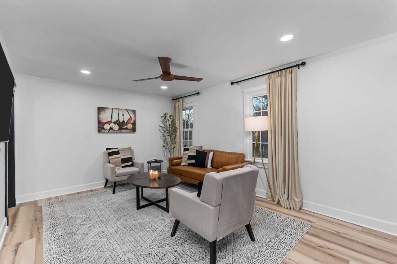 Un salon moderne avec un canapé en cuir marron, deux fauteuils, une table basse et un ventilateur de plafond.