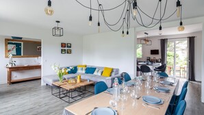 A modern dining area with a long table set for six, a gray sofa with colorful cushions, and a wooden console table with a vase of flowers. - 4 bedroom lovely home in Cancale (Cancale)