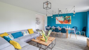 A modern living room with a gray sofa, a wooden coffee table, and a dining area with blue chairs and a large abstract painting. - 4 bedroom lovely home in Cancale (Cancale)