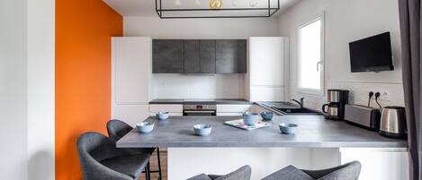A modern kitchen with a central island, bar stools, a built-in oven, and a flat-screen TV mounted above the island.