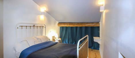 Quarto com cama, mesas de cabeceira, viga de madeira no teto e janela com cortinas.
