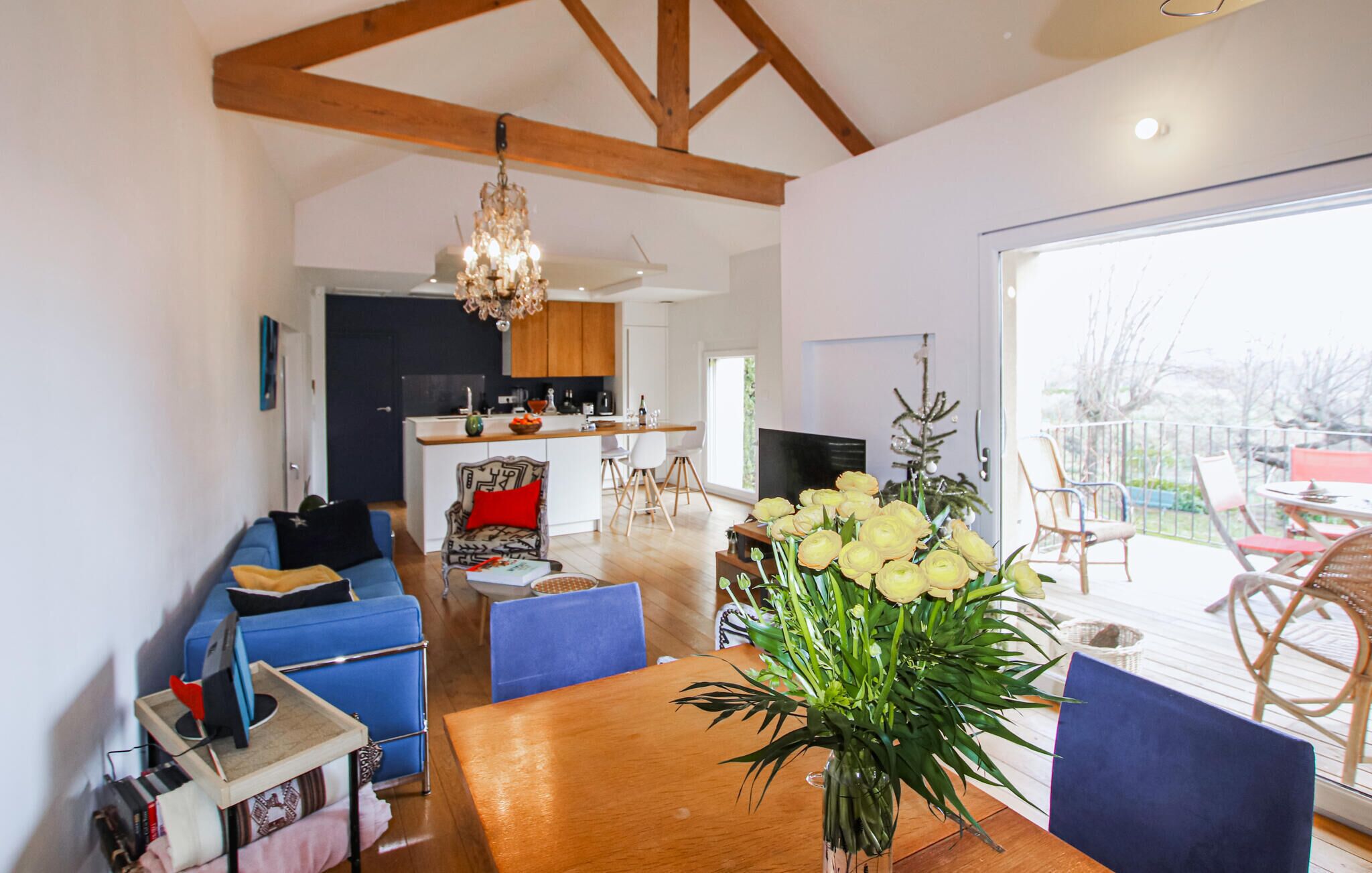 A modern living room with a wooden dining table, blue sofas, and a chandelier.