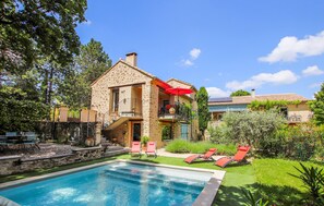 Een stenen huis met zwembad, terras en tuin.