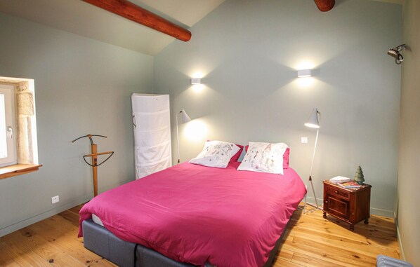 Een slaapkamer met een bed, twee bedlampen, een nachtkastje, een raam en een houten plafondbalk.