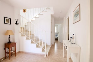 Eine Treppe führt zu einer zweiten Etage, ein kleiner Tisch mit einer Lampe und ein an der Wand befestigter Kleiderhaken.