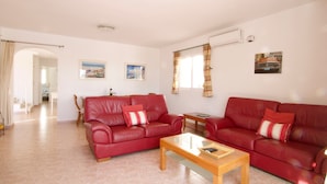 Ein Wohnzimmer mit zwei roten Ledersofas, einem Holztisch und einem Essbereich im Hintergrund.