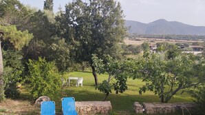 Ein Garten mit zwei blauen Stühlen, einer Steinmauer und Blick auf ferne Hügel.