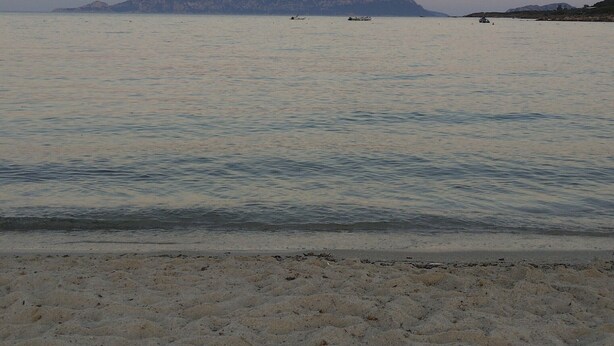 Ein Strand mit ruhigem Wasser, einem entfernten Berg und einem klaren Himmel.