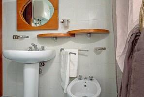 A bathroom with a white sink, a mirror, a bidet, and wooden shelves. - Apartment in a villa surrounded by Gallura countryside, close to the sea (Olbia)