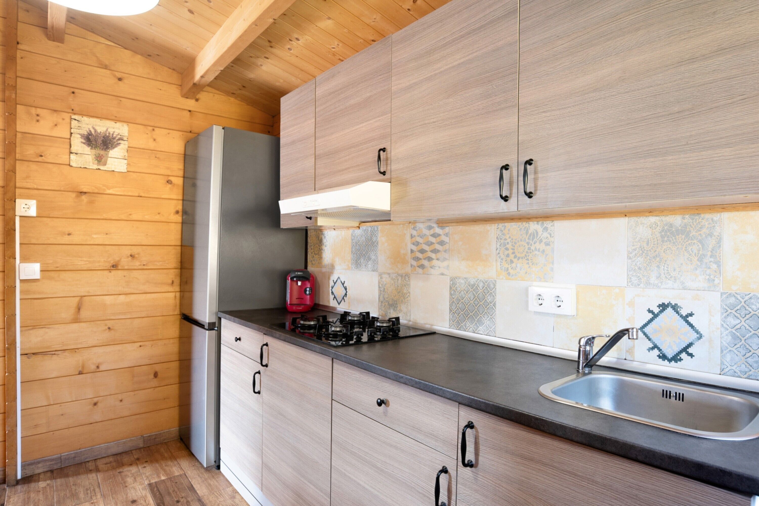 Een keuken met houten kastjes, een roestvrijstalen spoelbak en een rode waterkoker.