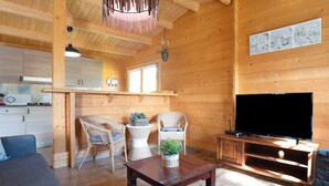 A wooden interior with a sofa, two wicker chairs, a table with a plant, a TV, and a kitchen area. - Rural House with Private Pool near Dehesa Montenmedio – Sunshine Tour, Vejer (Vejer de la frontera)