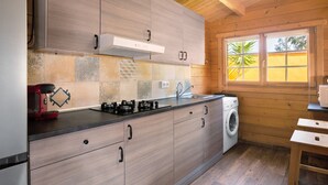 A modern kitchen with wooden cabinets, a built-in stove, a washing machine, and a window with a view of greenery. - Rural House with Private Pool near Dehesa Montenmedio – Sunshine Tour, Vejer (Vejer de la frontera)