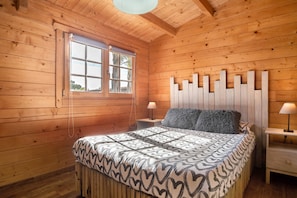 Ein Zimmer mit Holzwänden, einem Bett, zwei Nachttischen, einem Fenster und einer Deckenleuchte.