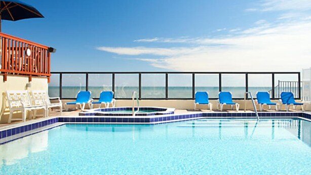 A pool area with blue chairs and a view of the ocean.