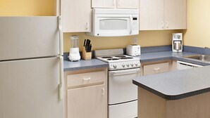 A kitchen with white appliances, including a refrigerator, microwave, stove, and toaster. There is a coffee maker and a blender on the counter.