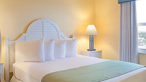 A hotel room with a large bed, white headboard, and a nightstand with a lamp.