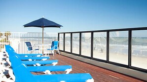 A deck with blue lounge chairs and a large umbrella, overlooking a beach.
