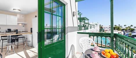 A balcony with a table set for breakfast, a green door, and a view of the neighborhood.