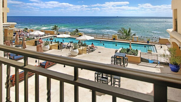 A pool area with lounge chairs and umbrellas, overlooking the ocean.