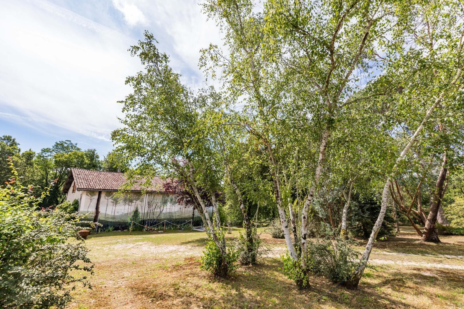 A rustic building with a tiled roof, surrounded by a garden with various trees and shrubs.
