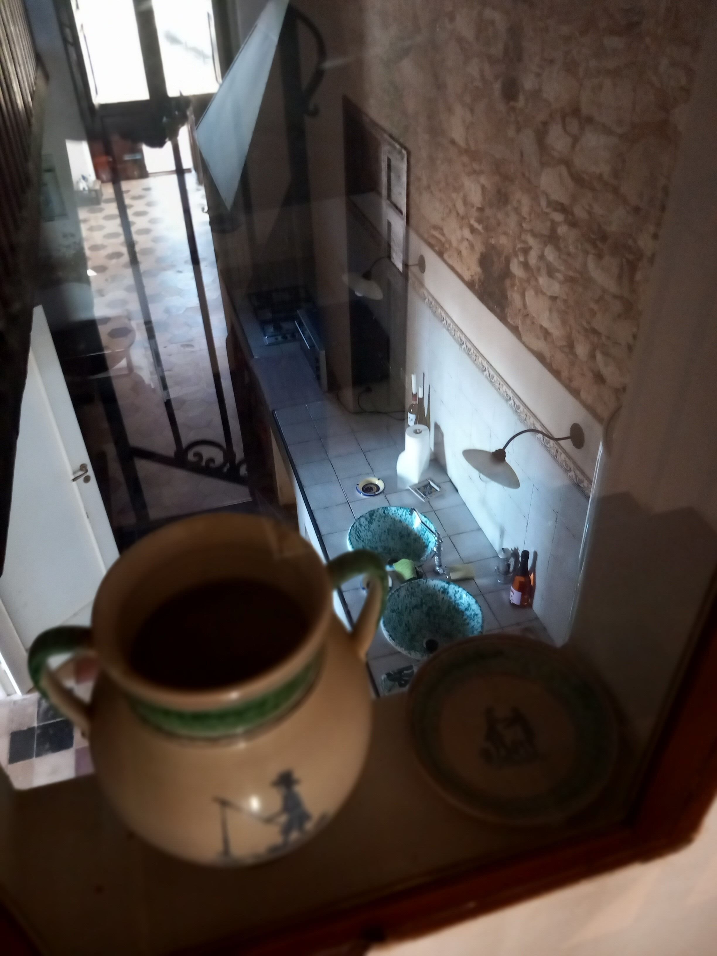 Et køkken med en kaffemaskine på et bord, klinkegulv og et vindue i baggrunden.