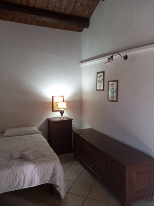 Un dormitorio con cama, mesita de noche con lámpara, cómoda y dos cuadros en la pared.
