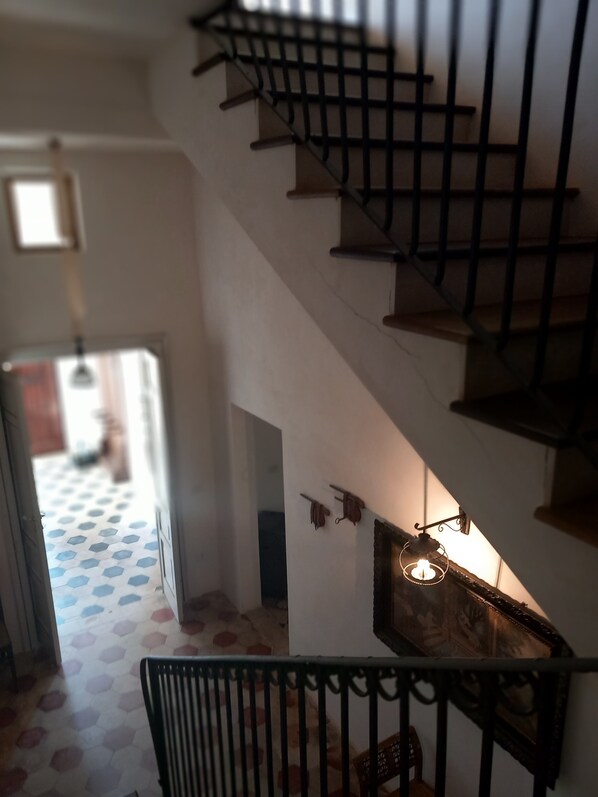 Una escalera con barandilla de metal, piso estampado y lámpara colgante.