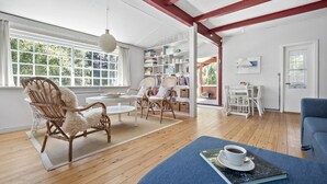 Un salón amplio con un ventanal grande, piso de madera y una estantería llena de libros y objetos decorativos.
