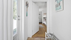 Un pasillo con suelo de madera, una puerta blanca y un banco con zapatos. Hay un cartel en la pared que dice 'CHILL BLISS CALM RELAX'.