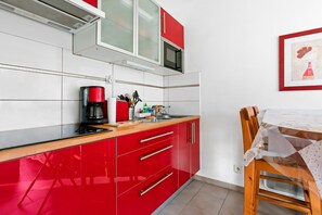 A kitchen with red cabinets, a microwave, a coffee maker, and a wooden dining table with a white tablecloth. - Apartment 'Boulouris' with Private Terrace, Wi-Fi and Air Conditioning (Saint-Raphaël)