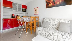 Ett kompakt bostadsutrymme med ett litet kök, en matplats och en soffa med mönstrat tyg.