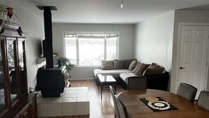 A modern living room with a dining area, a fireplace, and a large window providing natural light. - Cozy Country Living (Nipawin)