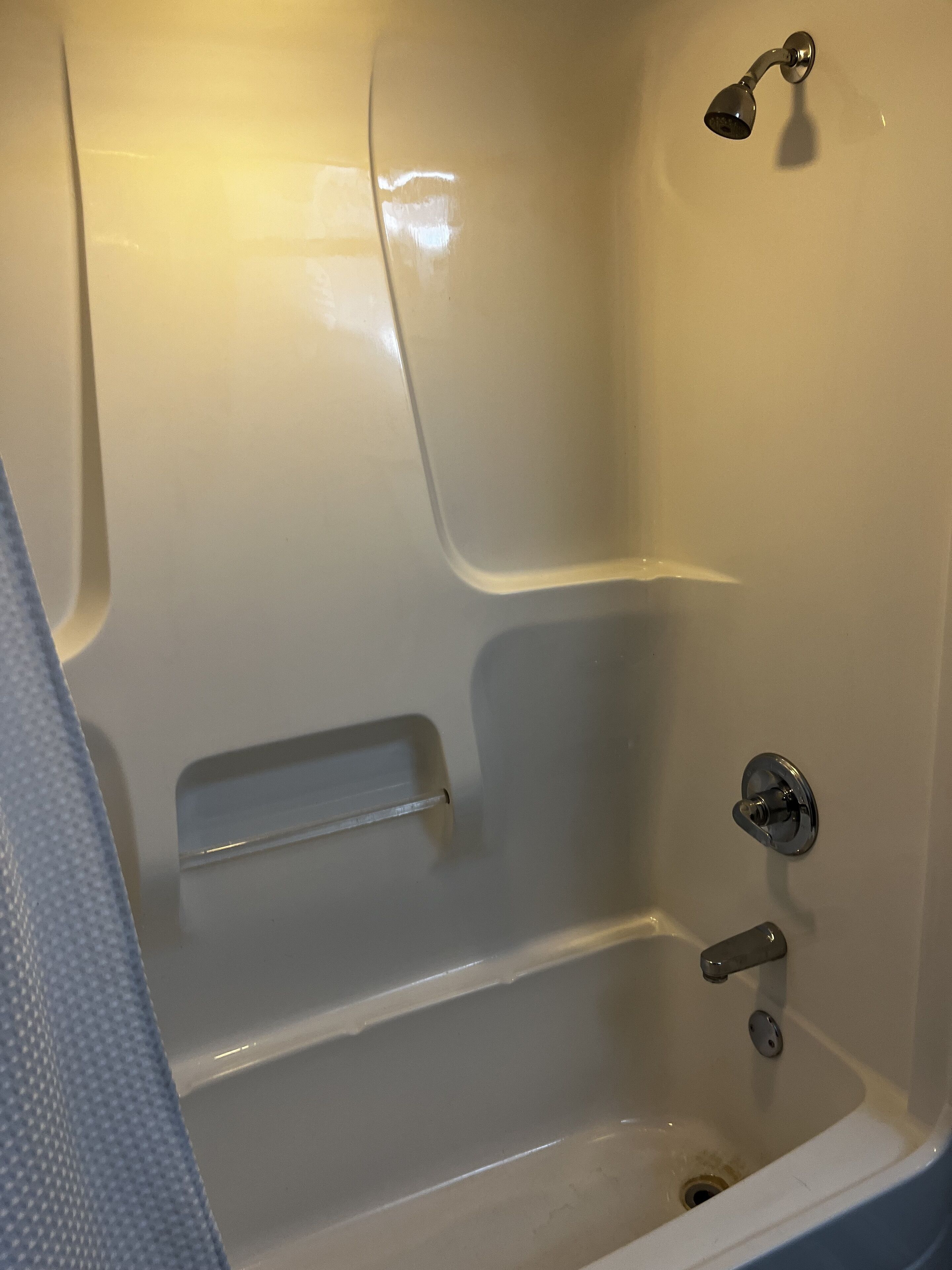 Une baignoire équipée d’un pommeau de douche, d’une étagère intégrée et d’un drain.