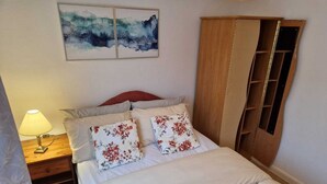 A bedroom with a bed, a nightstand, a lamp, a wardrobe, and a painting on the wall. - Cozy Room A @ Shiremoor (Shiremoor)