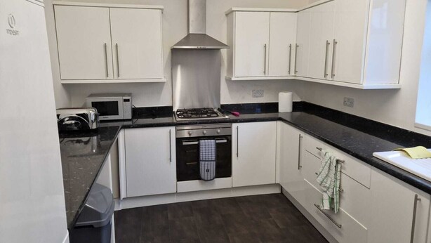 A compact kitchen with white cabinets, a stainless steel range hood, a microwave, and a gas stove. - Cozy Room A @ Shiremoor (Shiremoor)
