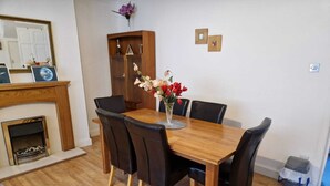 A dining area with a wooden table, black chairs, a vase with flowers, a fireplace, and a mirror on the wall. - Cozy Room A @ Shiremoor (Shiremoor)