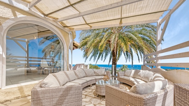 A covered outdoor seating area with wicker furniture, a palm tree, and a view of the ocean. - Villa Adriana with Sea View, Mountain View, Wi-Fi and Air Conditioning (Dénia)