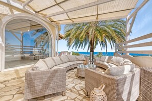 A covered outdoor seating area with wicker furniture, a palm tree, and a view of the ocean.