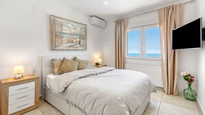 A bedroom with a bed, bedside lamps, a painting, a TV, and a window with curtains. - Villa Adriana with Sea View, Mountain View, Wi-Fi and Air Conditioning (Dénia)