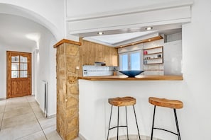 Una cocina con armarios de madera, un pilar de piedra, un tazón azul sobre la encimera y dos taburetes.