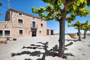A stone building with multiple windows and a door, a tree with a hammock, and a clear sky.