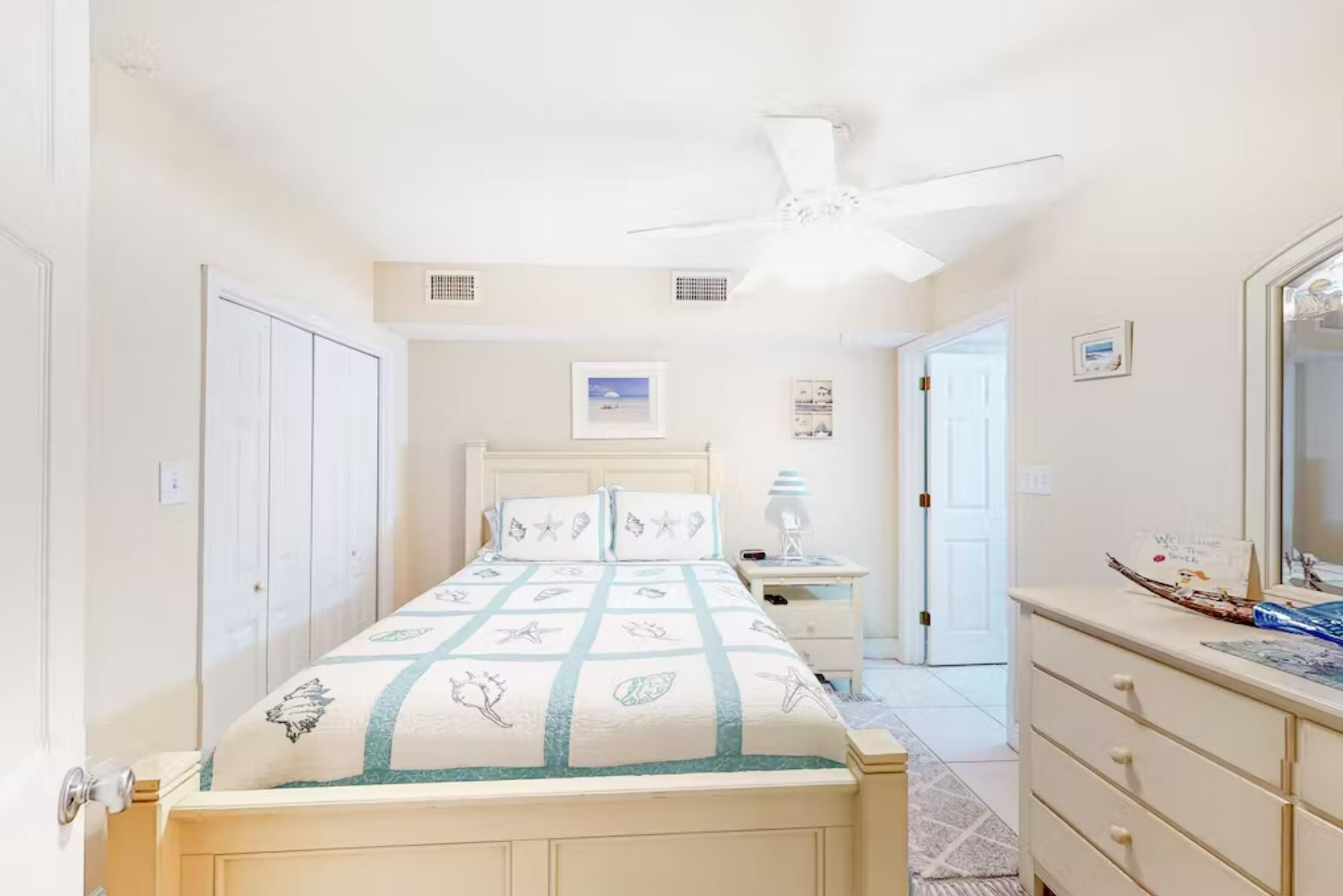 A bedroom with a bed, a nightstand, a dresser, a ceiling fan, and a door.