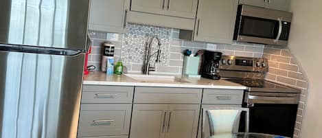 A modern kitchen with grey cabinets, stainless steel appliances, a glass dining table, and a blue glass bowl.