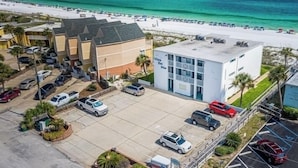 Vue aérienne d’un hôtel avec un parking, une plage et l’océan en arrière-plan.