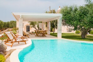 Zona de piscina con sillones de descanso, un área de estar cubierta y vistas al paisaje circundante.