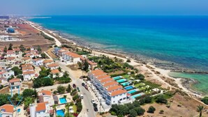 An aerial view of a coastal residential area with houses, a beach, and clear blue waters. - Villa Posidonia - 200m from Sandy Beach (Ayia Napa)